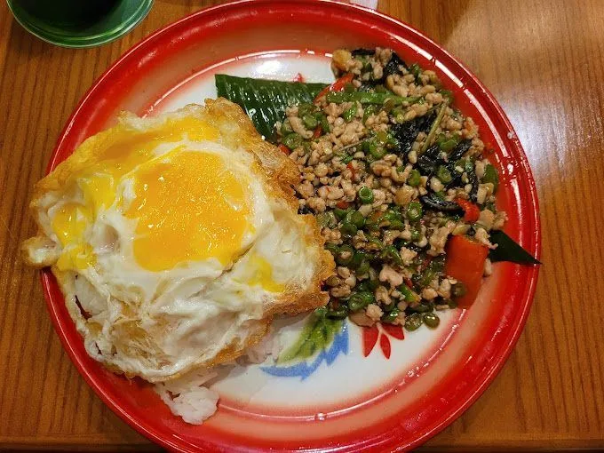 Thai basil pork rice with a crispy fried egg on an enamel plate